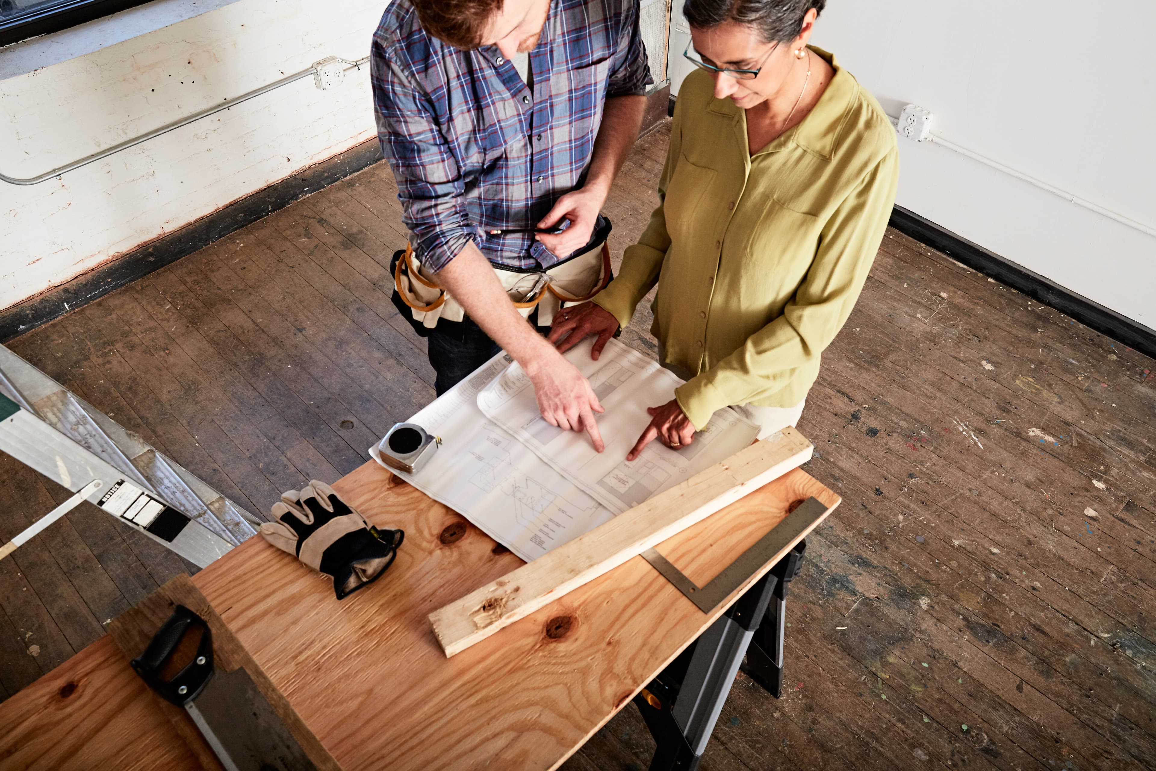 Dos personas revisando planos sobre un banco de trabajo de madera.